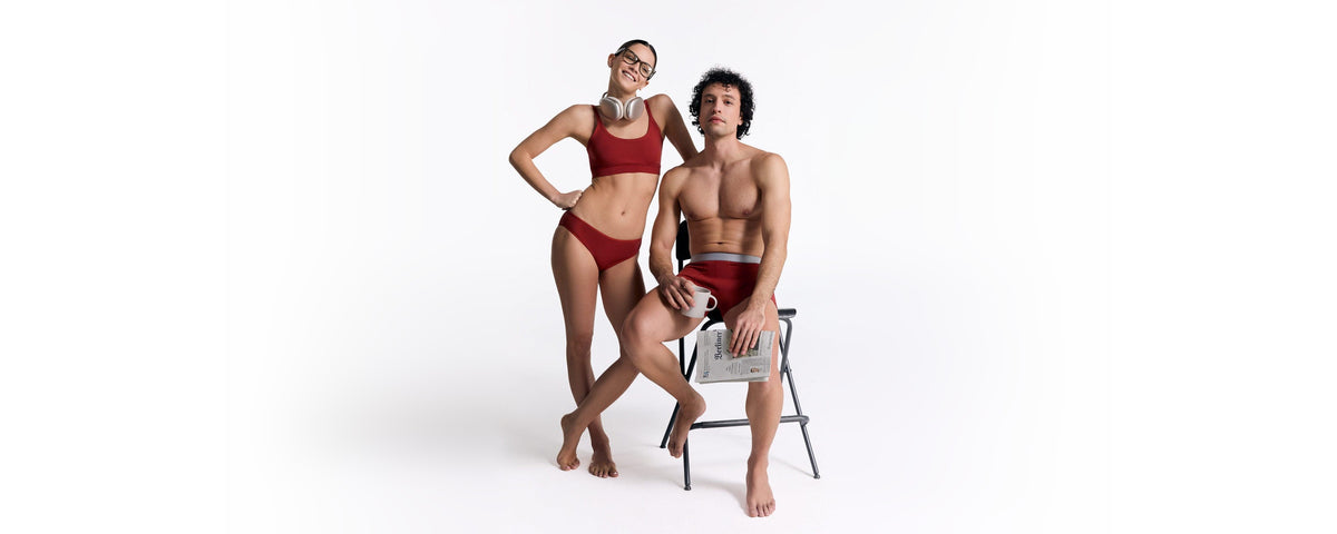 Two models in matching red swimwear posing with a magazine on a white studio background.